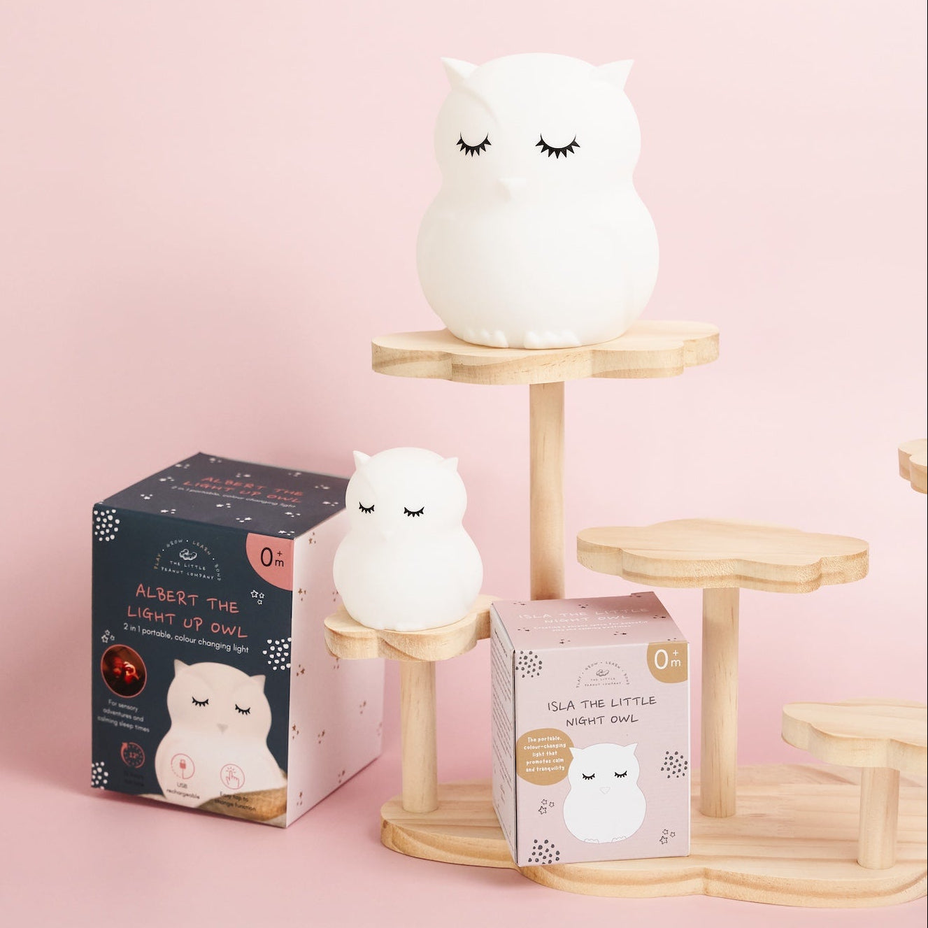 White owl-shaped night light on a wooden stand with packaging on a pink background